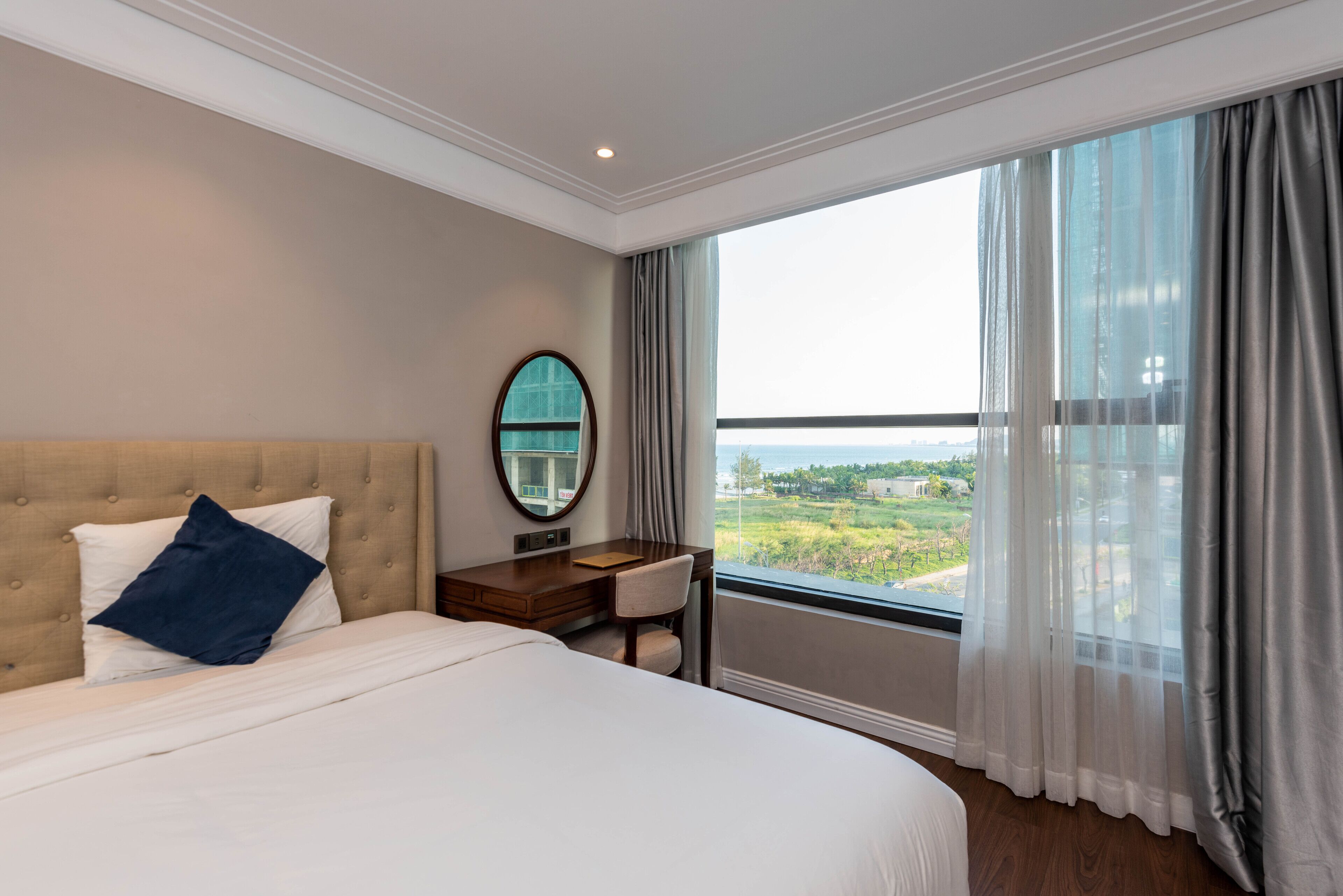 A hotel room with a large bed, a desk, a chair, a mirror, and a window with a view of the outdoors.