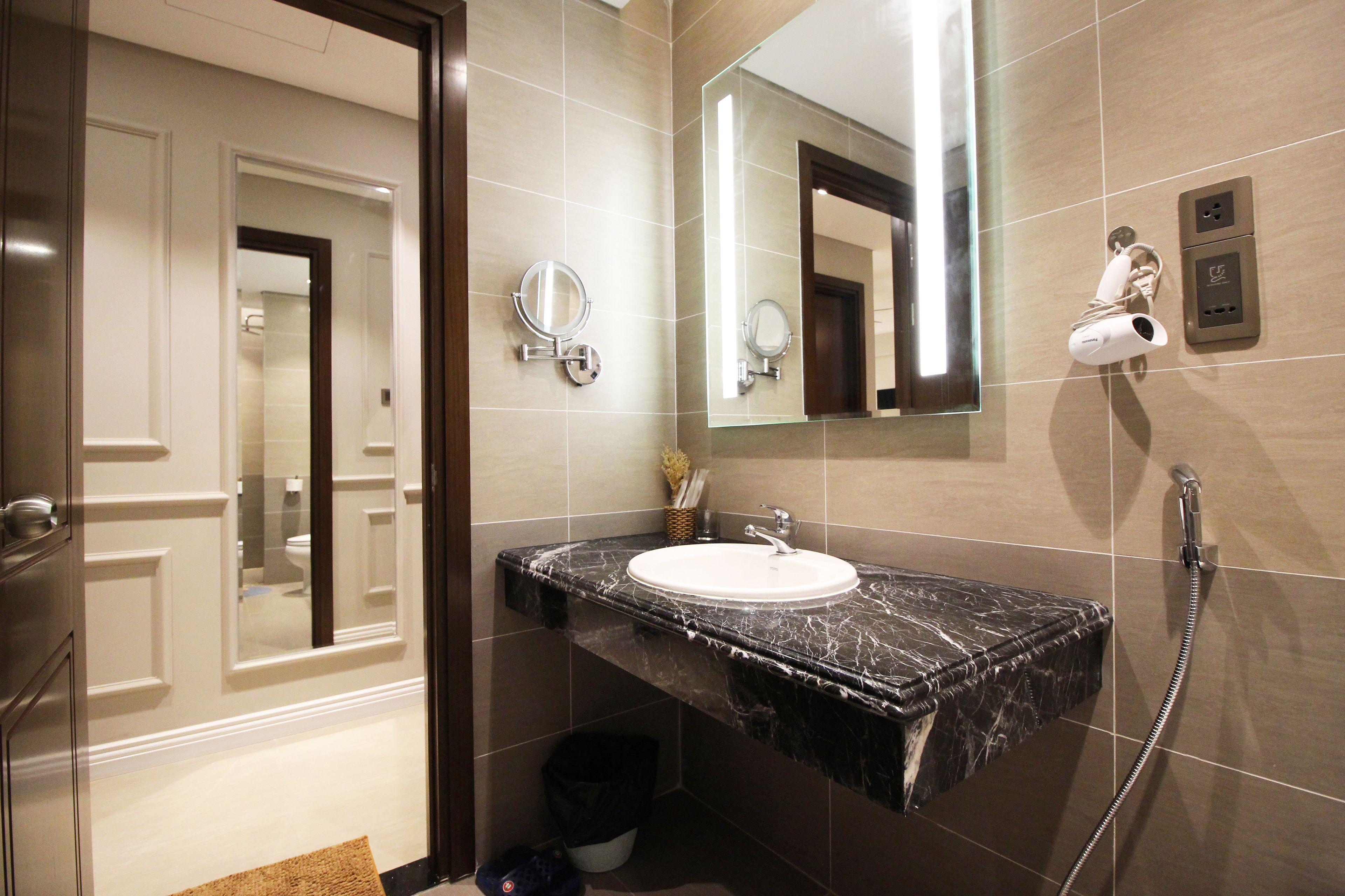 A bathroom with a marble sink, a mirror, a handheld showerhead, and a towel rack.