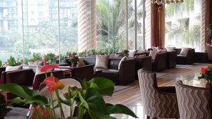 A spacious indoor area with multiple seating arrangements, large windows offering a view of greenery and buildings, and a variety of potted plants. - Guangzhou Yihe Hotel (Guangzhou)
