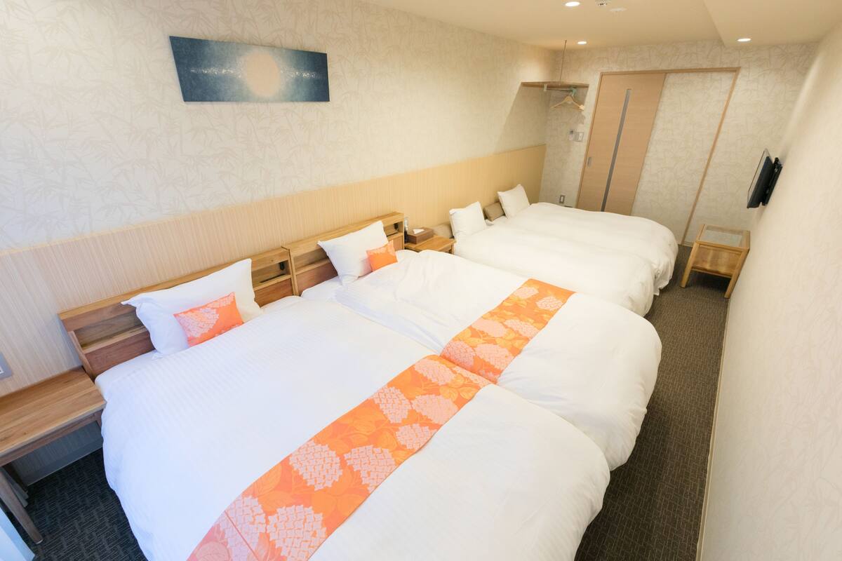 A hotel room with two beds, a wooden headboard, a nightstand, a wall-mounted TV, and a painting.