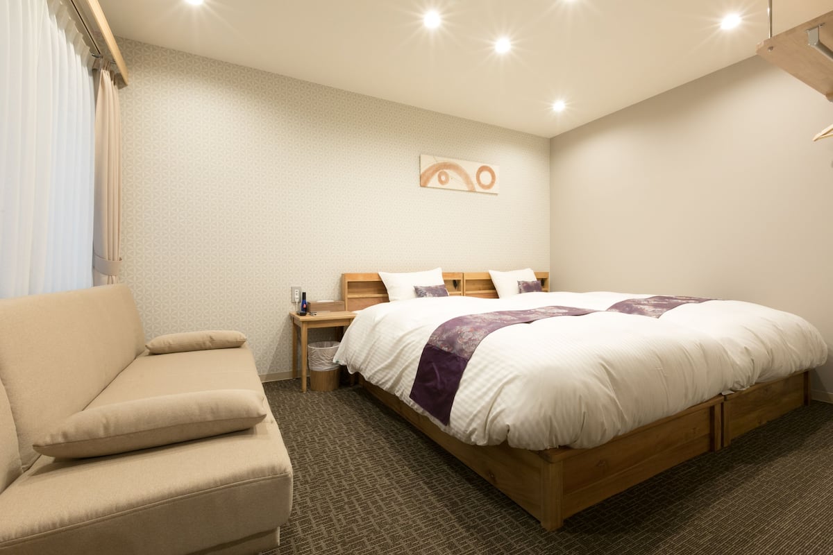A hotel room with a bed, a sofa, a nightstand, and a wall-mounted artwork.