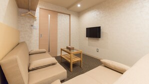 A modern room with a sofa, a small wooden table, a TV mounted on the wall, and a door with a wooden frame. - Stay SAKURA Kyoto Gyoen East (Kyoto)