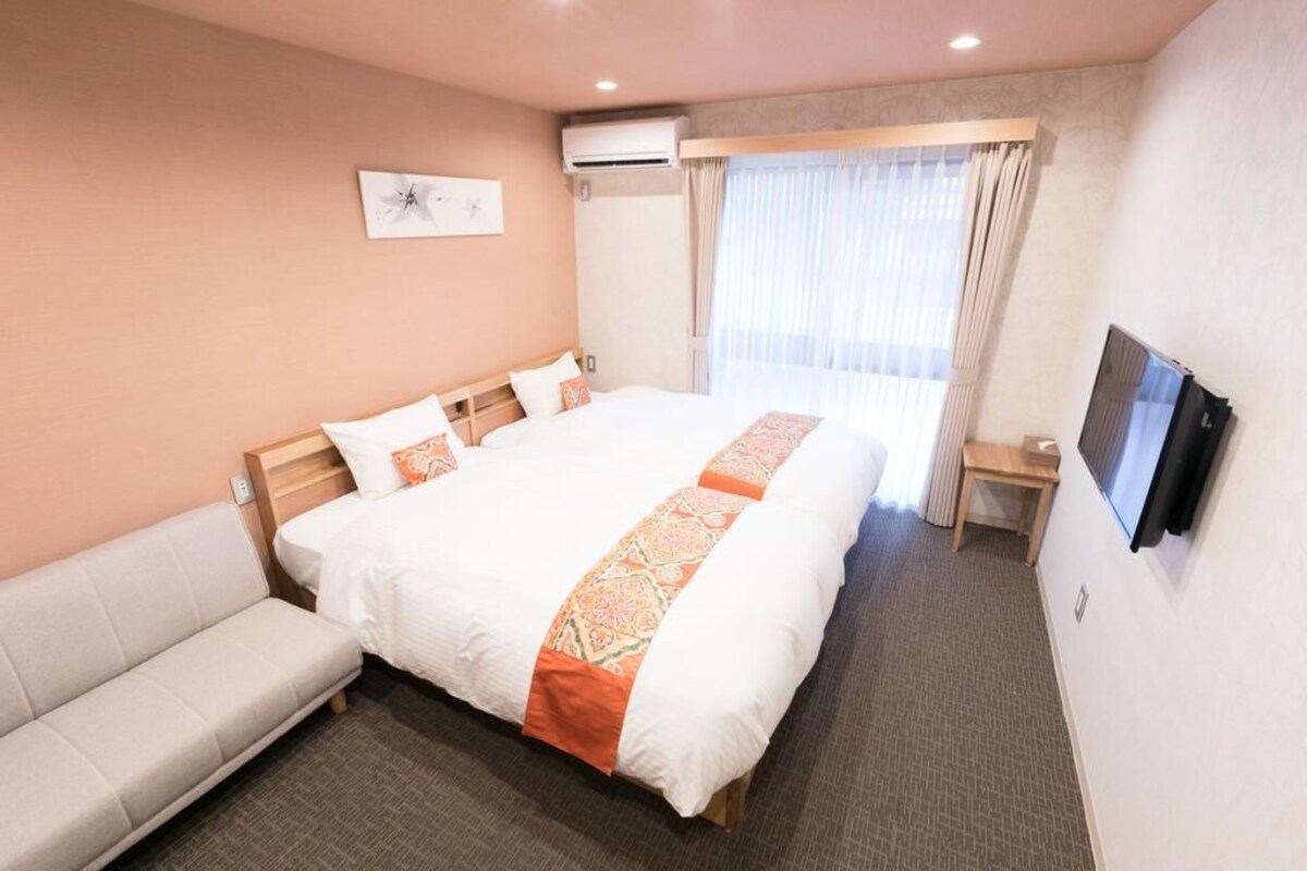 A hotel room with a large bed, a sofa, a TV, and a window with curtains.