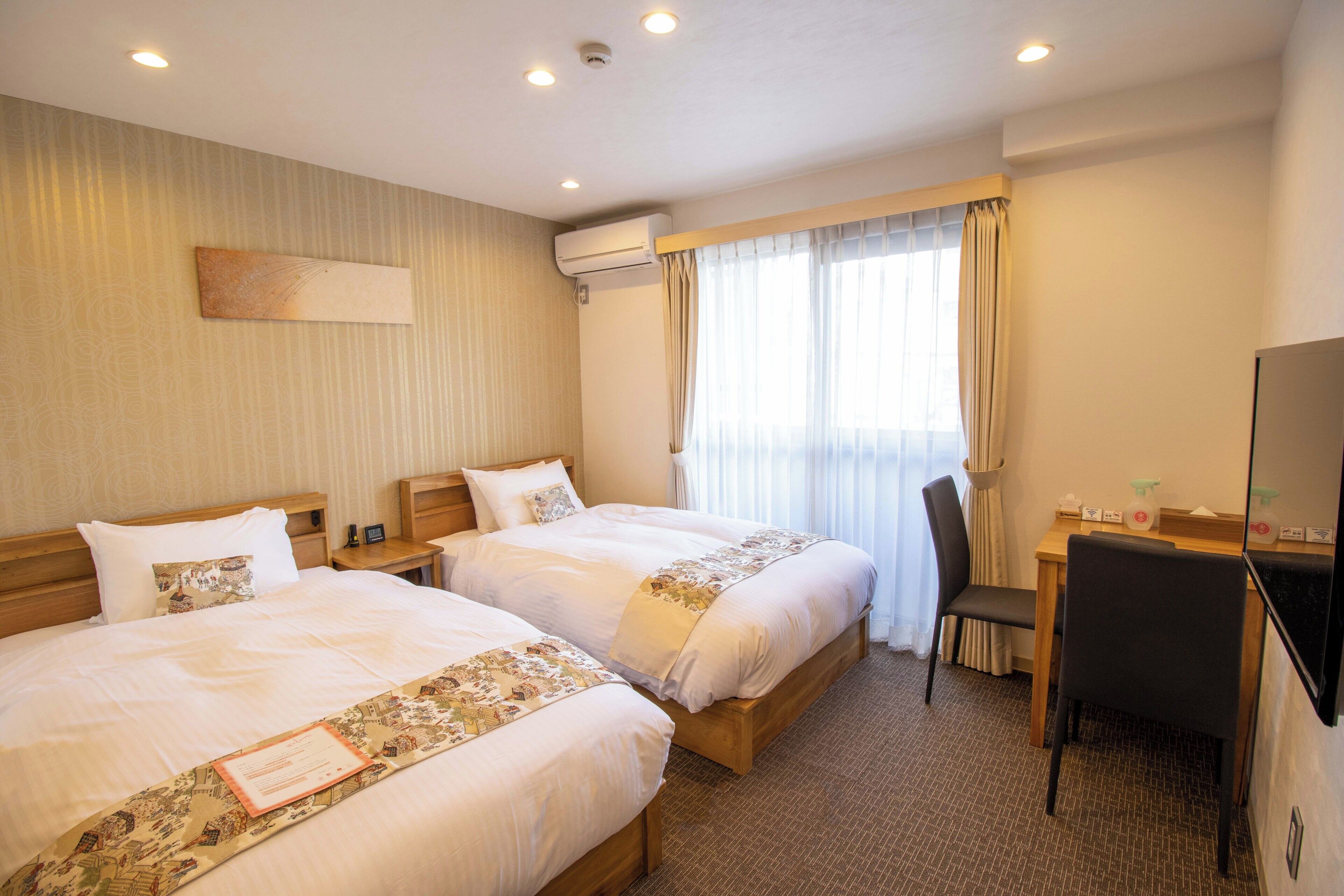 Quarto de hotel com duas camas, uma escrivaninha, uma cadeira e uma televisão.