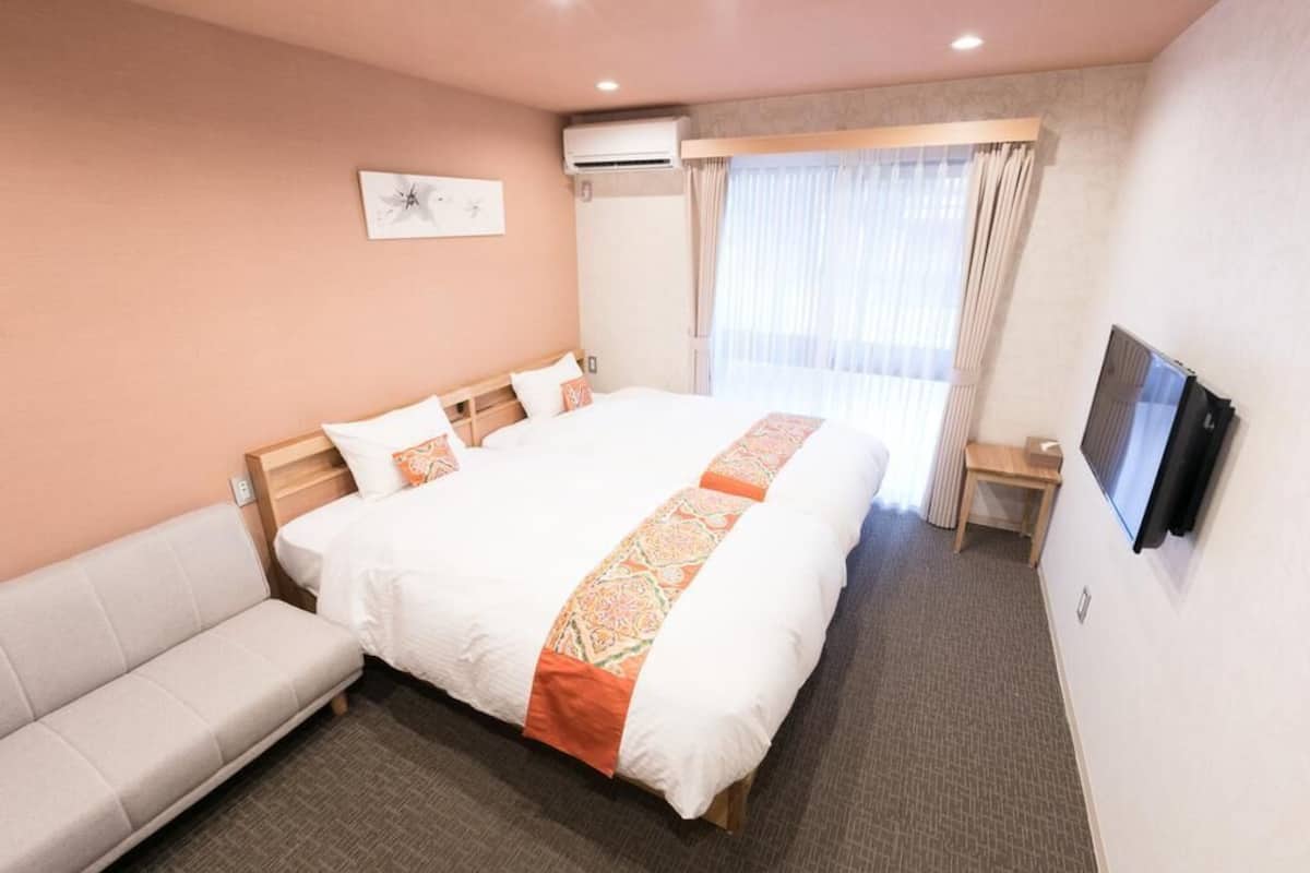 A hotel room with a large bed, a sofa, a TV, and a window with curtains.
