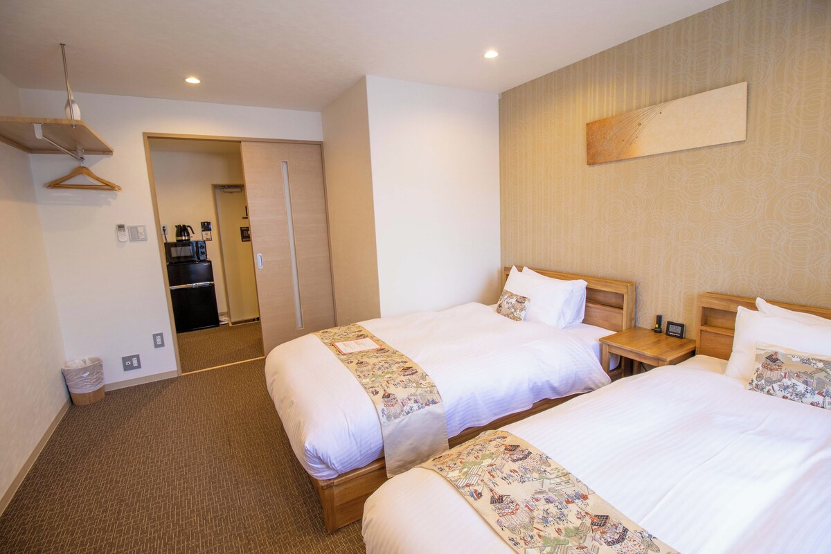 A hotel room with two beds, a wooden headboard, a small bedside table, and a wall-mounted artwork.