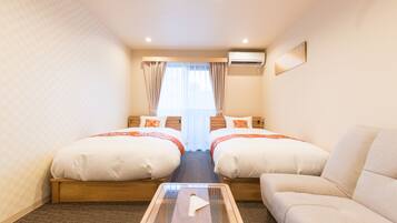 A hotel room with two beds, a sofa, a glass coffee table, and an air conditioning unit.