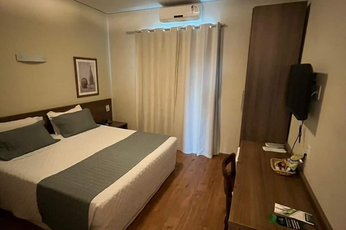 A hotel room with a bed, bedside table, and a desk with a chair.