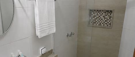 Un baño moderno con ducha de vidrio, inodoro, lavamanos y espejo.