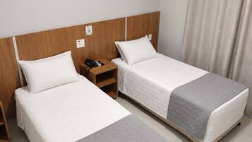 A hotel room with two single beds, a wooden headboard, a nightstand with a phone, and a window with curtains.