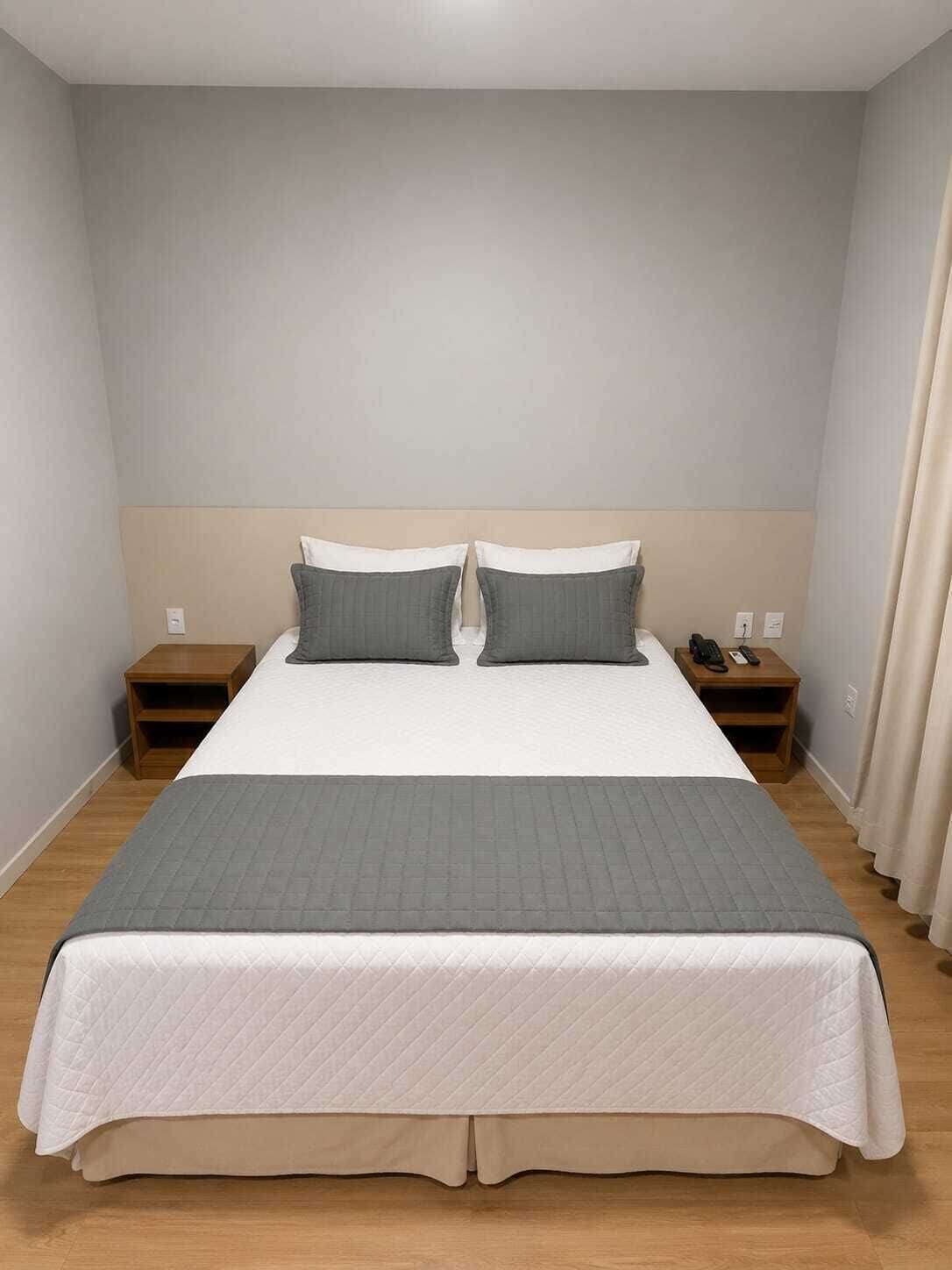 Una camera d'albergo standard con un letto, due comodini, un telefono e una tenda.