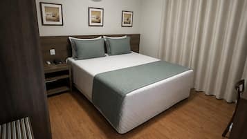 Una habitación de hotel con cama, mesitas de noche, un equipo de aire acondicionado y una ventana con cortinas.