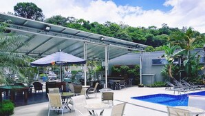 An outdoor pool area with lounge chairs and tables, surrounded by greenery and a covered seating area. - Hotel Serra de Jundiaí (Jundiai)