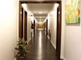 Un pasillo de hotel con pisos de madera, paredes blancas y un cuadro de tulipanes a la derecha.