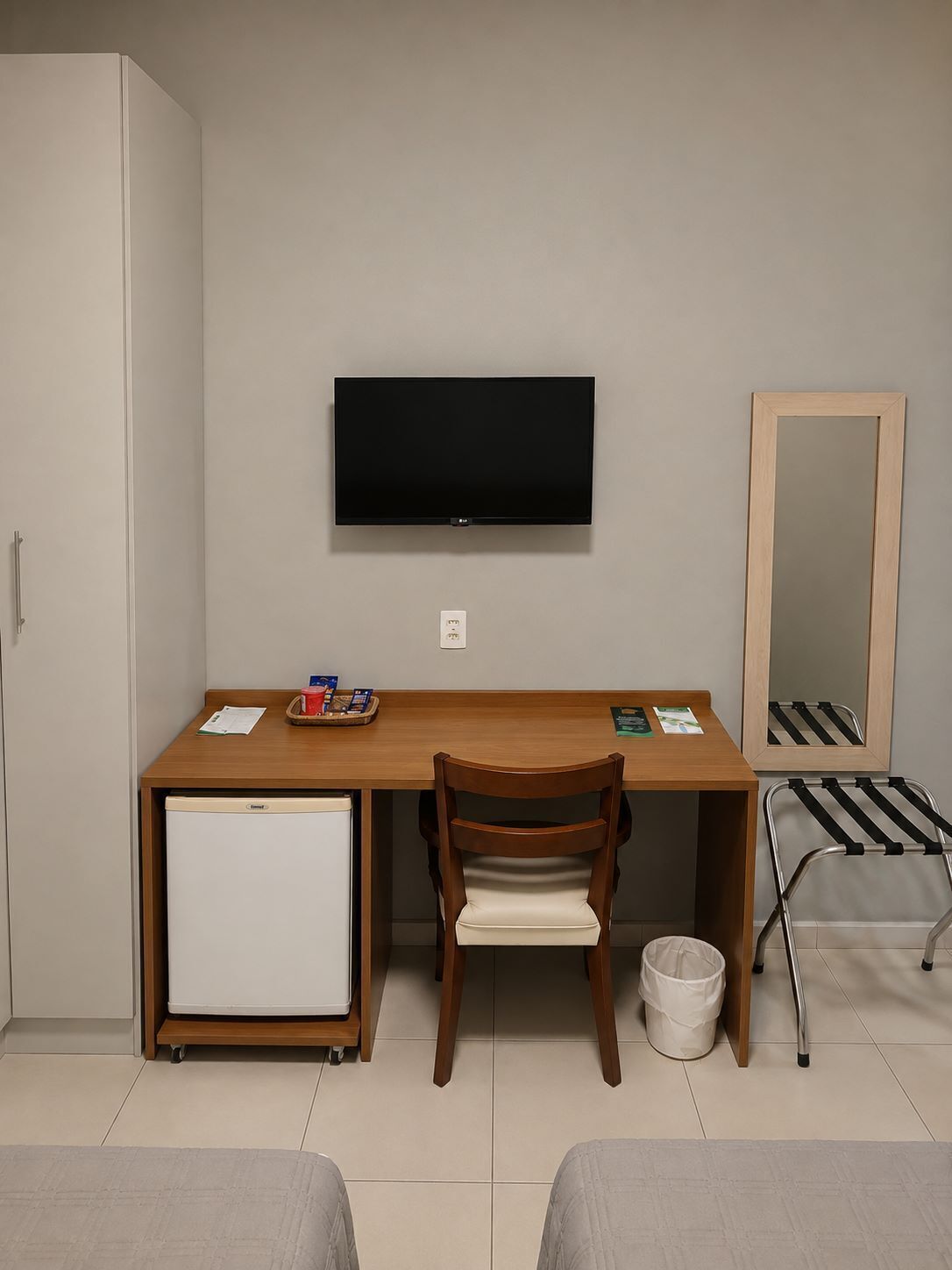 A compact room with a desk, chair, television, and a small refrigerator.
