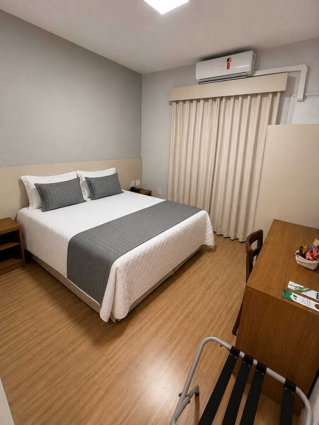Habitación de hotel con cama, mesita de noche, silla, escritorio y aire acondicionado.