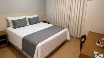 Habitación de hotel con cama, mesita de noche, silla, escritorio y aire acondicionado.