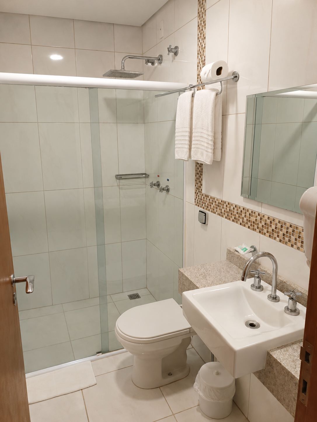 Un baño moderno con ducha separada por mampara de vidrio, inodoro, lavamanos y espejo.