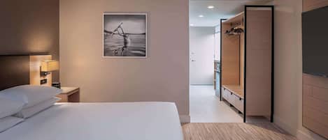 Habitación de hotel con cama, mesita de noche con lámpara, armario de madera y un cuadro en la pared.