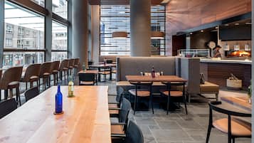 Un restaurante moderno con techos altos, ventanas amplias y una variedad de opciones de asientos, incluyendo mesas y cabinas.