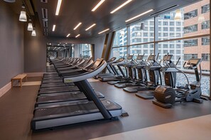 A gym with treadmills and elliptical machines, large windows, and a bench.