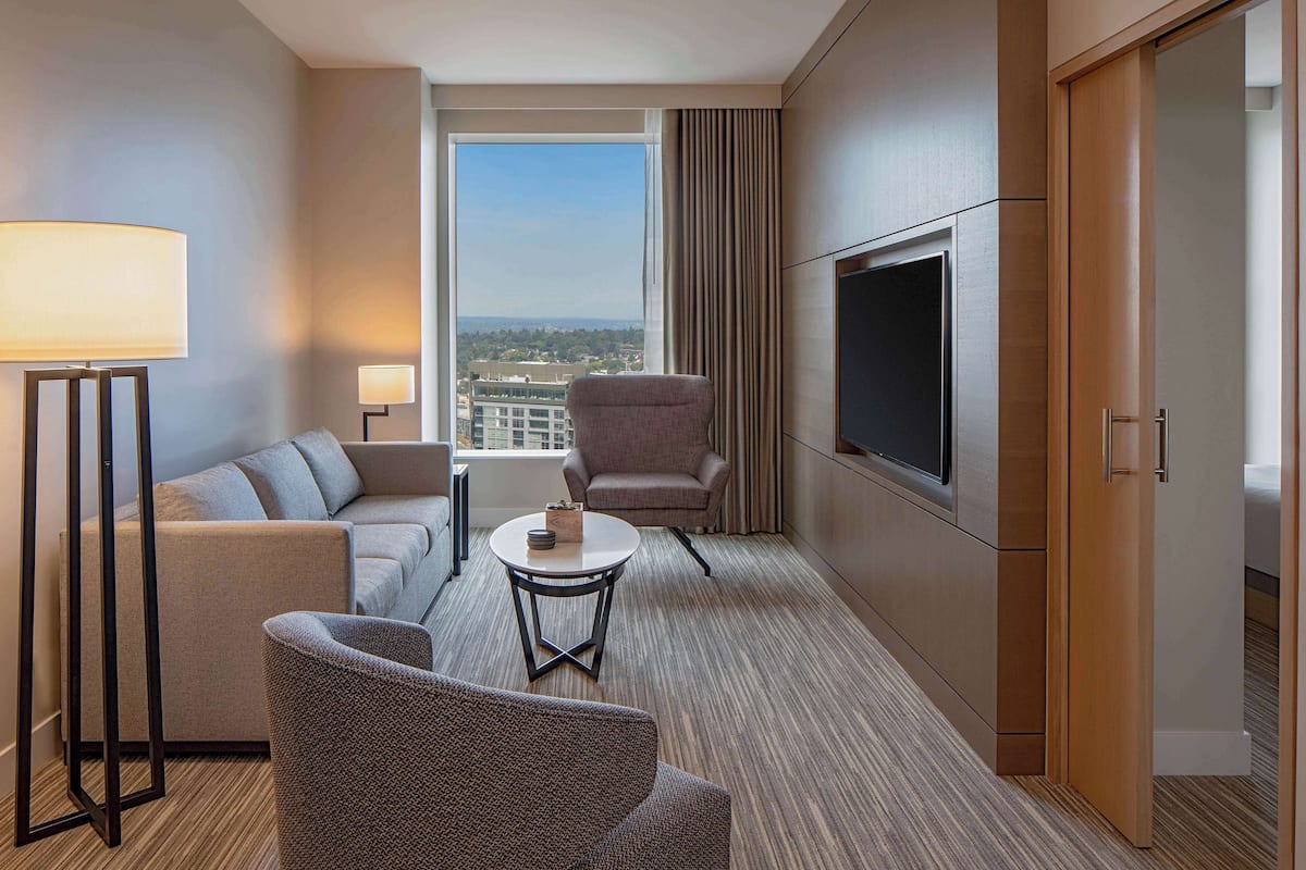 A hotel room with a sofa, armchair, small round table, and a TV.