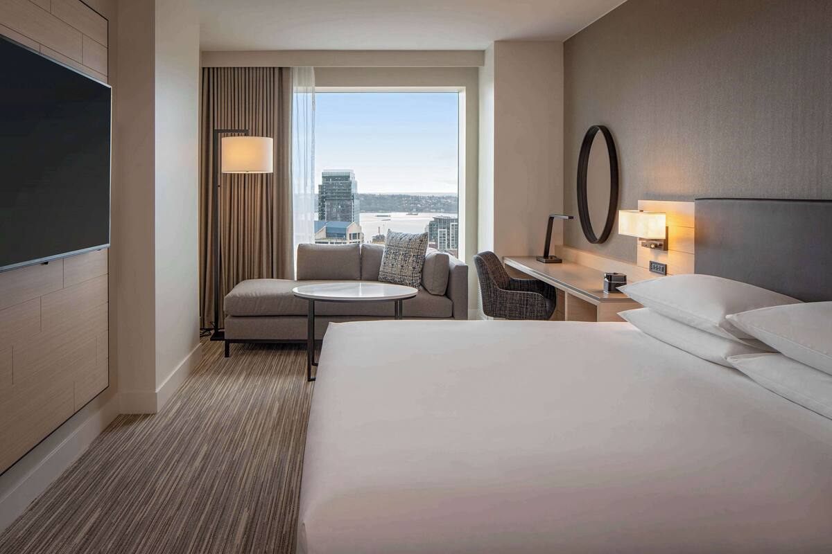 A hotel room with a large bed, a desk with a chair, a small round table, and a TV.