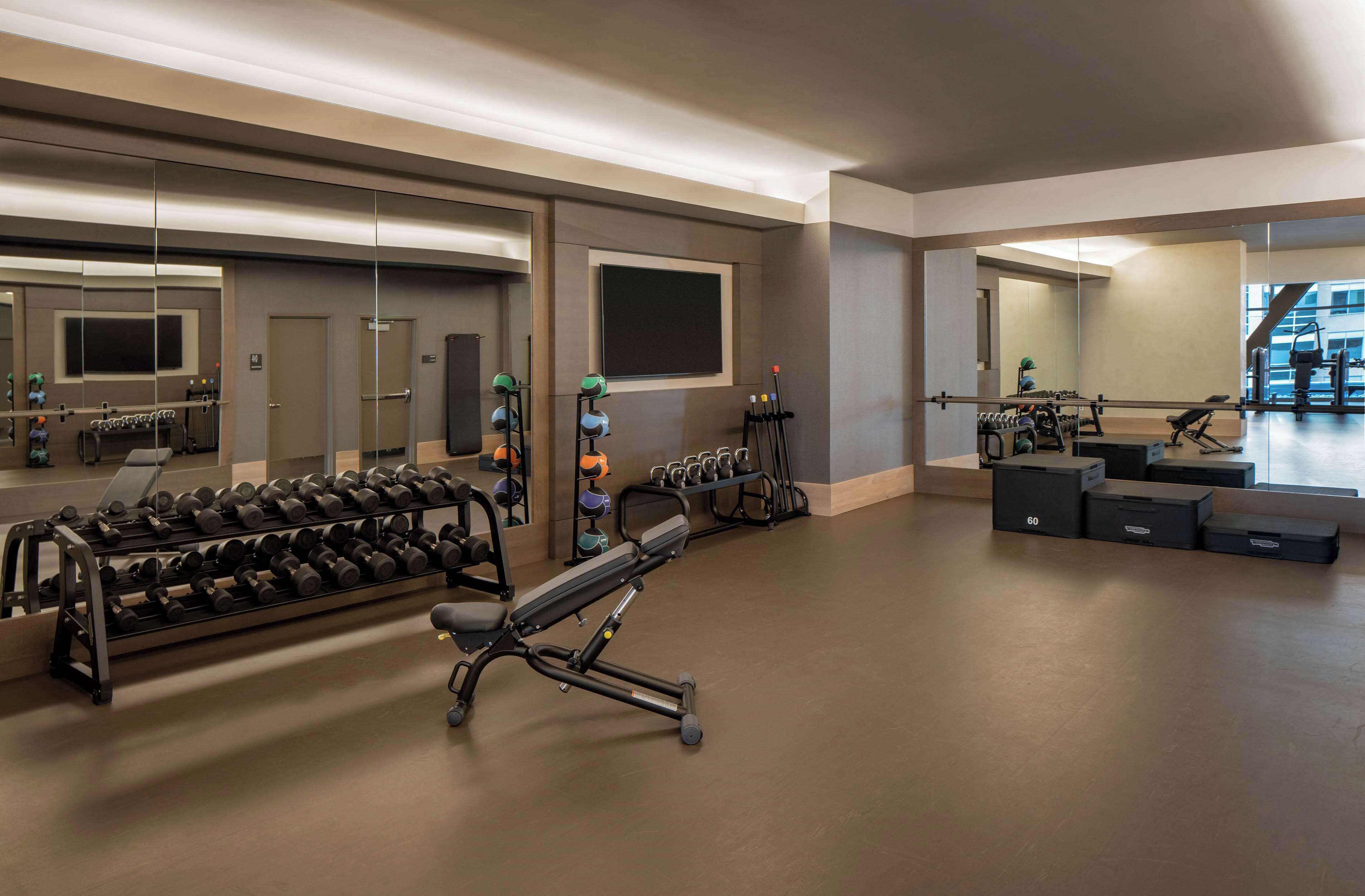 A gym with weightlifting equipment, mirrors, and a large window.