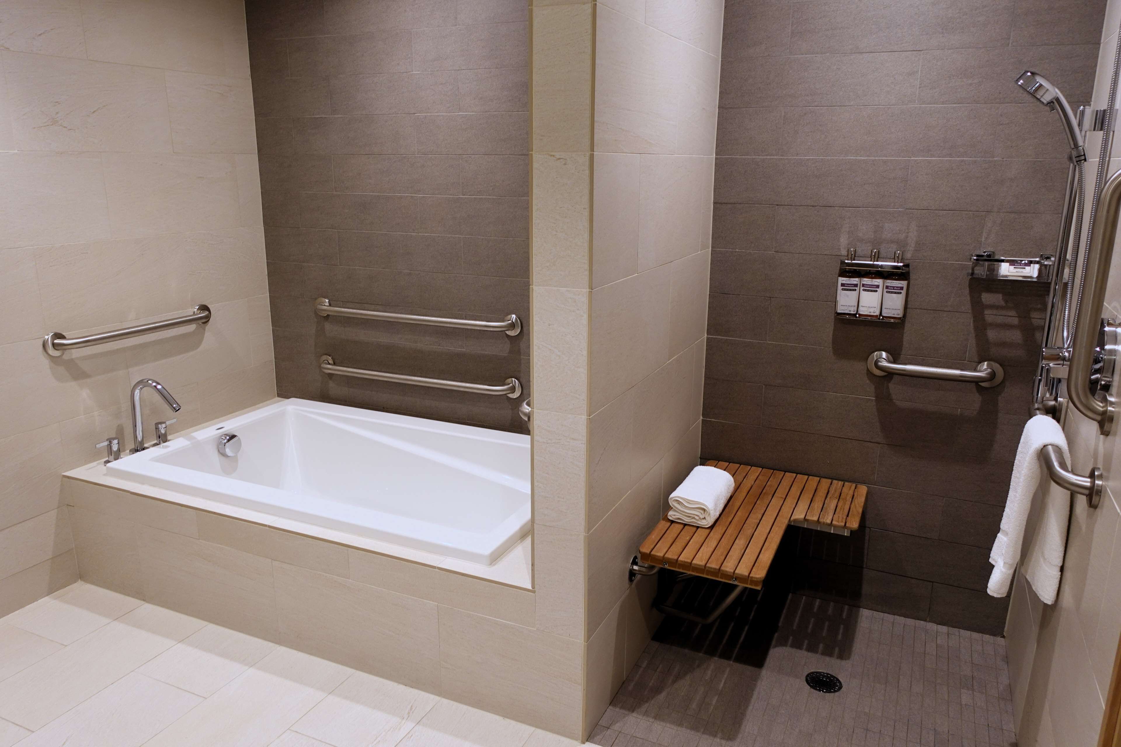 A modern bathroom with a bathtub, grab bars, a shower area, and a small wooden bench.