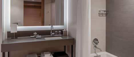 A modern bathroom with a large mirror, a sink, a bathtub, and a shelf with towels.