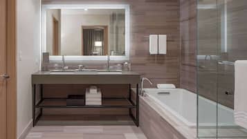 A modern bathroom with a large mirror, dual sinks, a glass-enclosed shower, and a built-in shelf with towels.