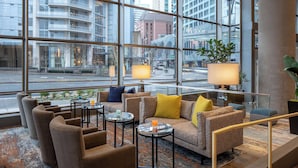 A modern hotel lobby with a large window offering a city view, comfortable seating, and a small table with a lamp. - Hyatt Regency Seattle (Seattle)