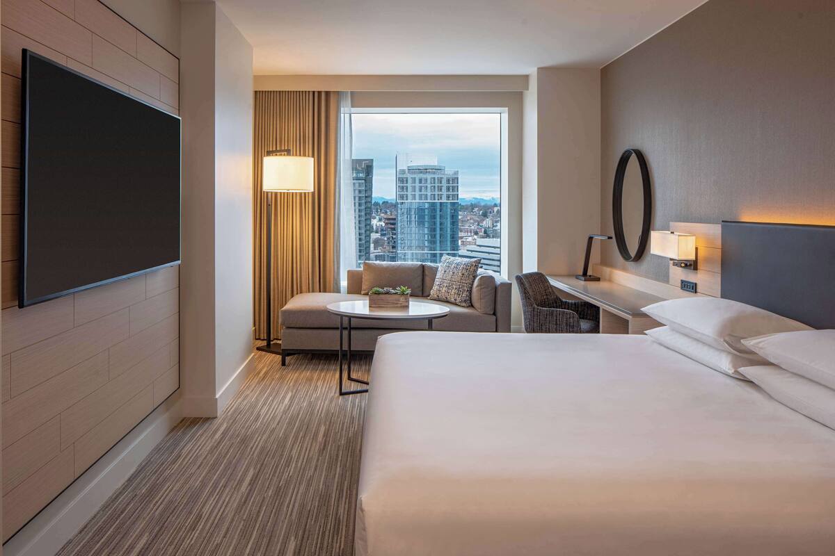 A hotel room with a large bed, a desk with a lamp, a sofa, and a TV mounted on the wall.