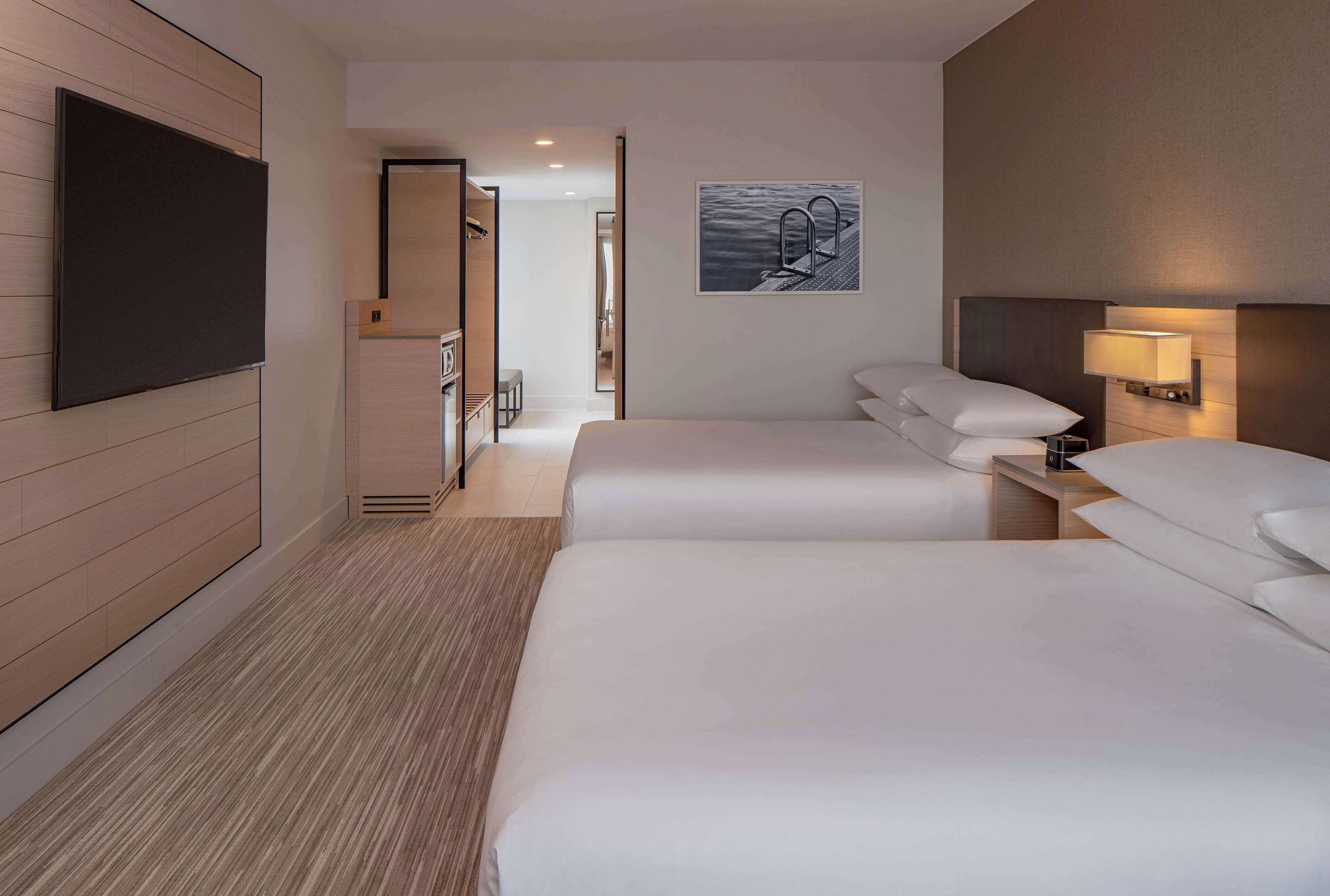 Une chambre d’hôtel avec deux lits, un téléviseur à écran plat, un tableau et une lampe de chevet.
