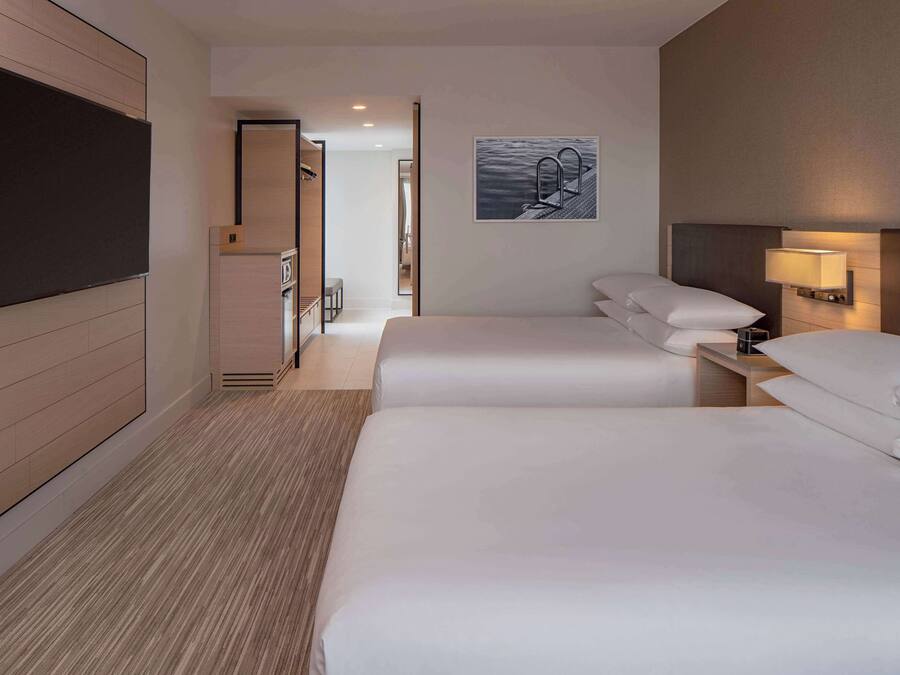 A hotel room with two beds, a flat-screen TV, a painting, and a bedside lamp.