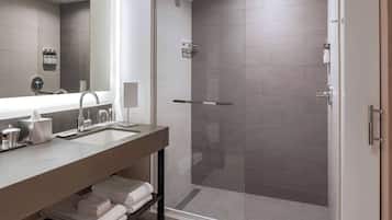 Une salle de bain moderne dotée d’une douche à parois de verre, d’un grand miroir et d’un meuble-lavabo avec un évier et un porte-serviettes.