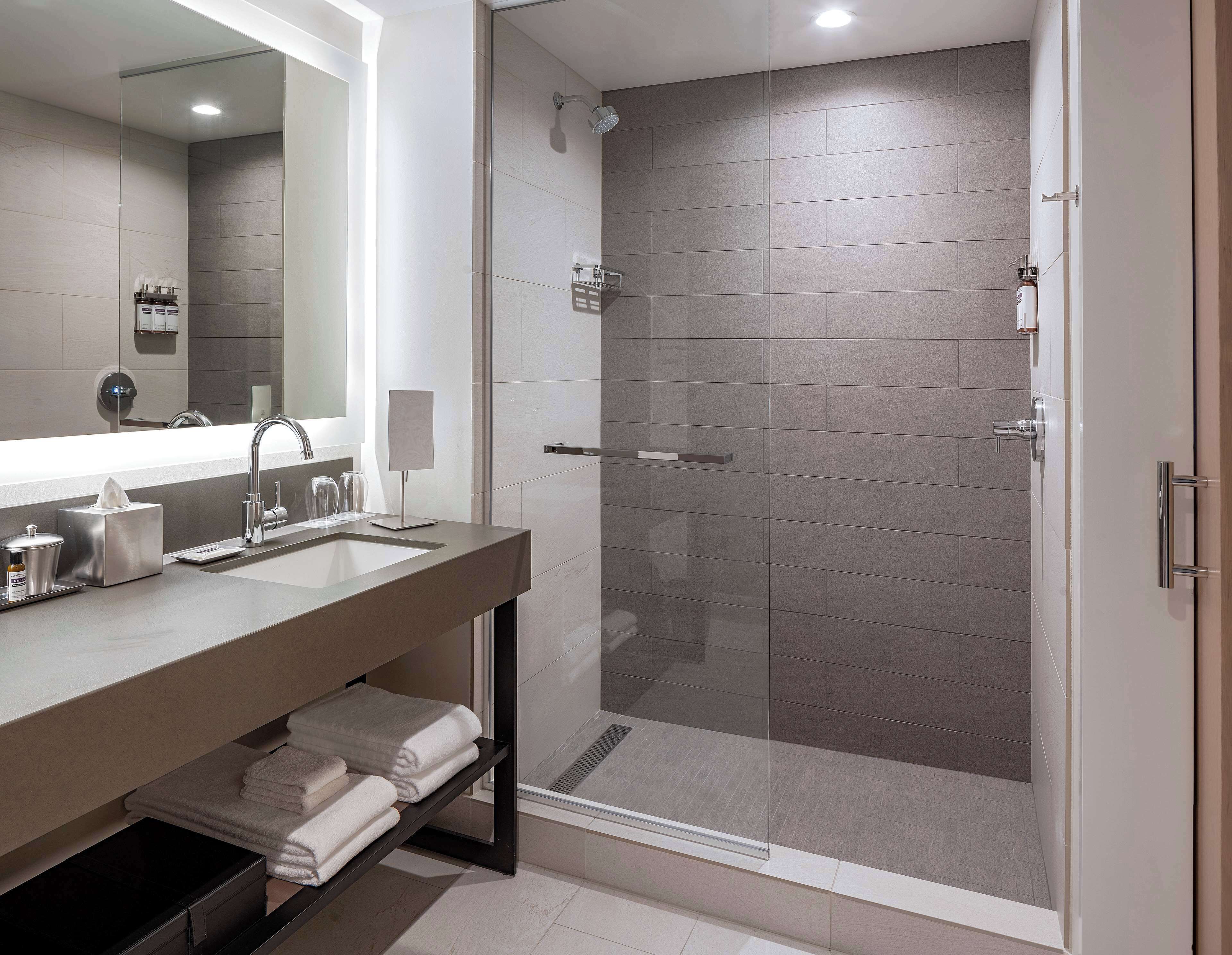 A modern bathroom with a glass-enclosed shower, a large mirror, and a vanity with a sink and towel rack.