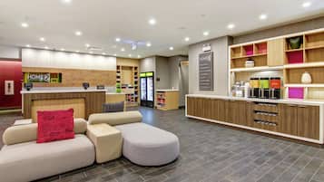 A modern hotel lobby with a reception desk, seating area, and a kitchen counter.