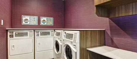 A laundry room with three washing machines and two dryers, wooden cabinets, and a white countertop.