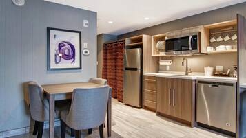 Una cocina moderna con microondas integrado, refrigerador de acero inoxidable y lavavajillas. Hay un comedor con mesa y sillas, y una cortina de ducha con estampado en zigzag.