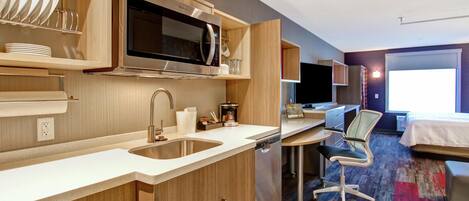 Una habitación de hotel moderna con kitchenette, un ventanal grande, una cama y un escritorio.