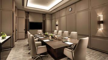 A conference room with a long table, chairs, a flat-screen TV, and wall-mounted lighting.