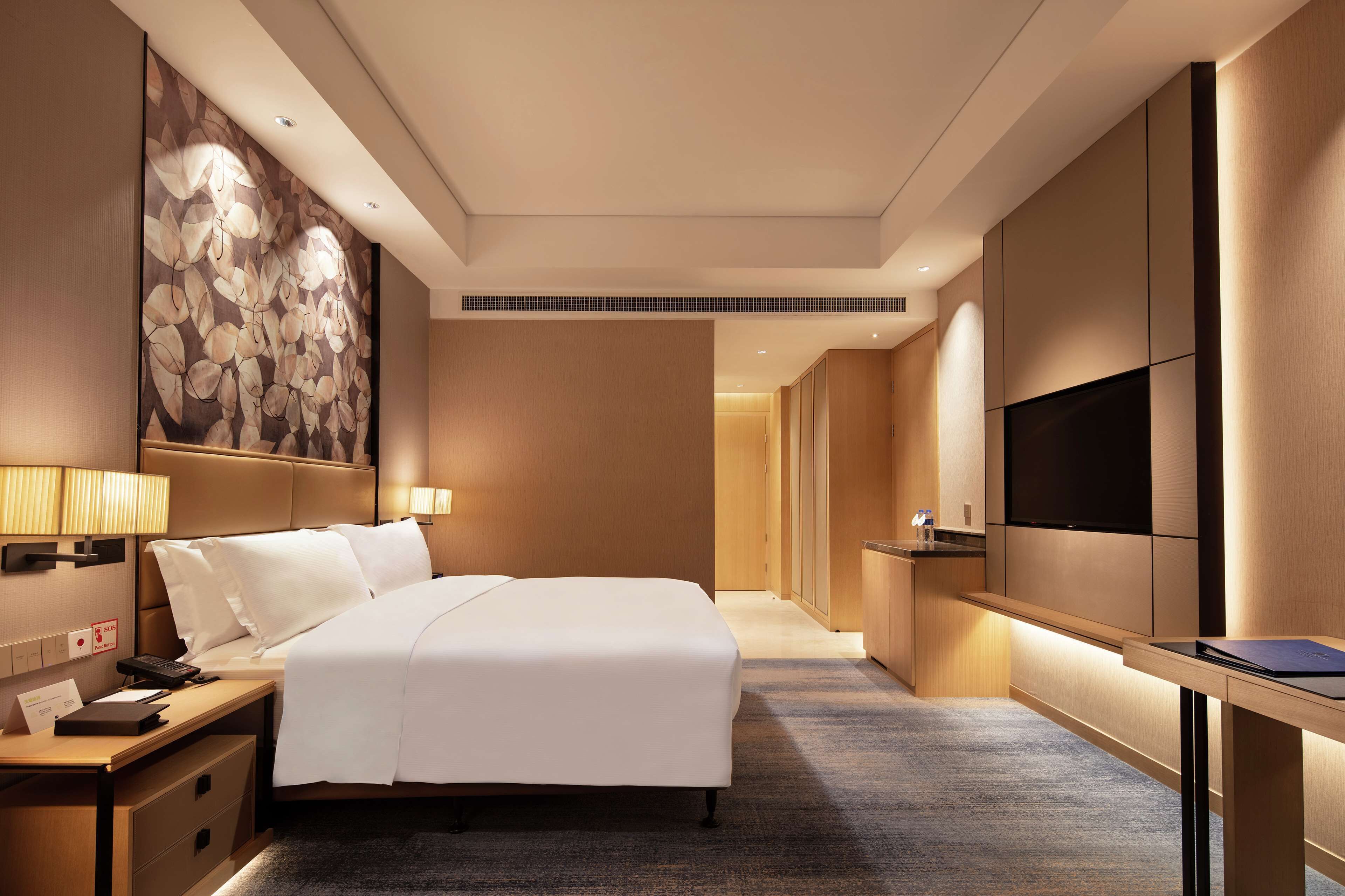 A hotel room with a large bed, bedside tables, a flat-screen TV, and a wall-mounted artwork.