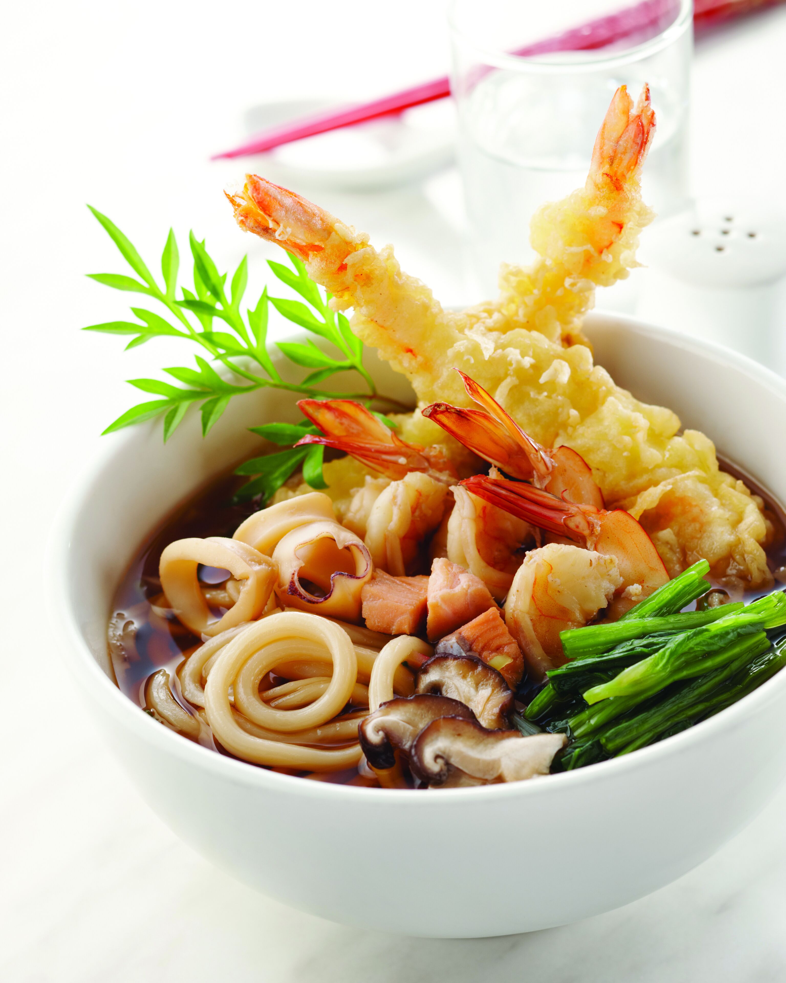 Un bol de ramen garni de divers ingrédients, notamment des nouilles, des légumes et des crevettes.