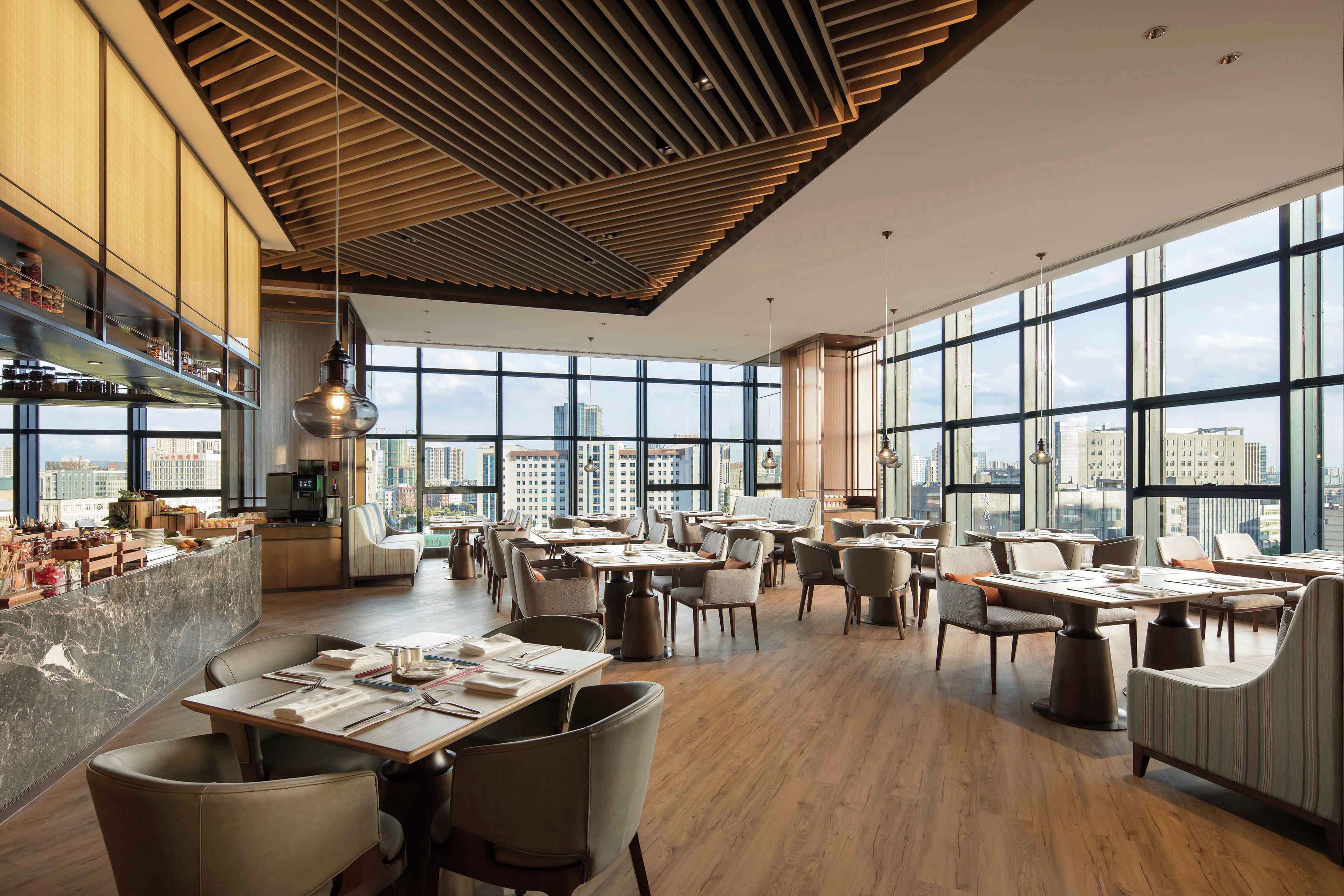 Un restaurante moderno con techos altos, amplias ventanas y vistas a la ciudad.