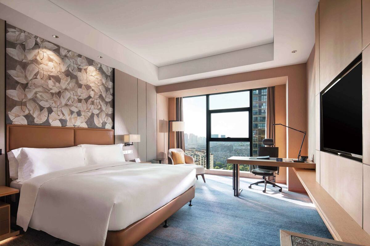 A modern hotel room with a large bed, a desk, a chair, and a TV.