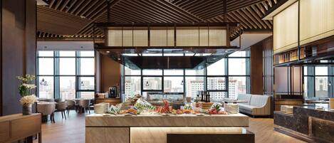 A spacious hotel lobby with a large reception desk, seating area, and large windows offering city views.
