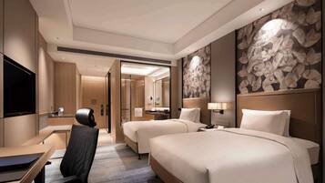 A hotel room with two beds, a desk, a chair, a TV, and a bathroom visible through an open door.