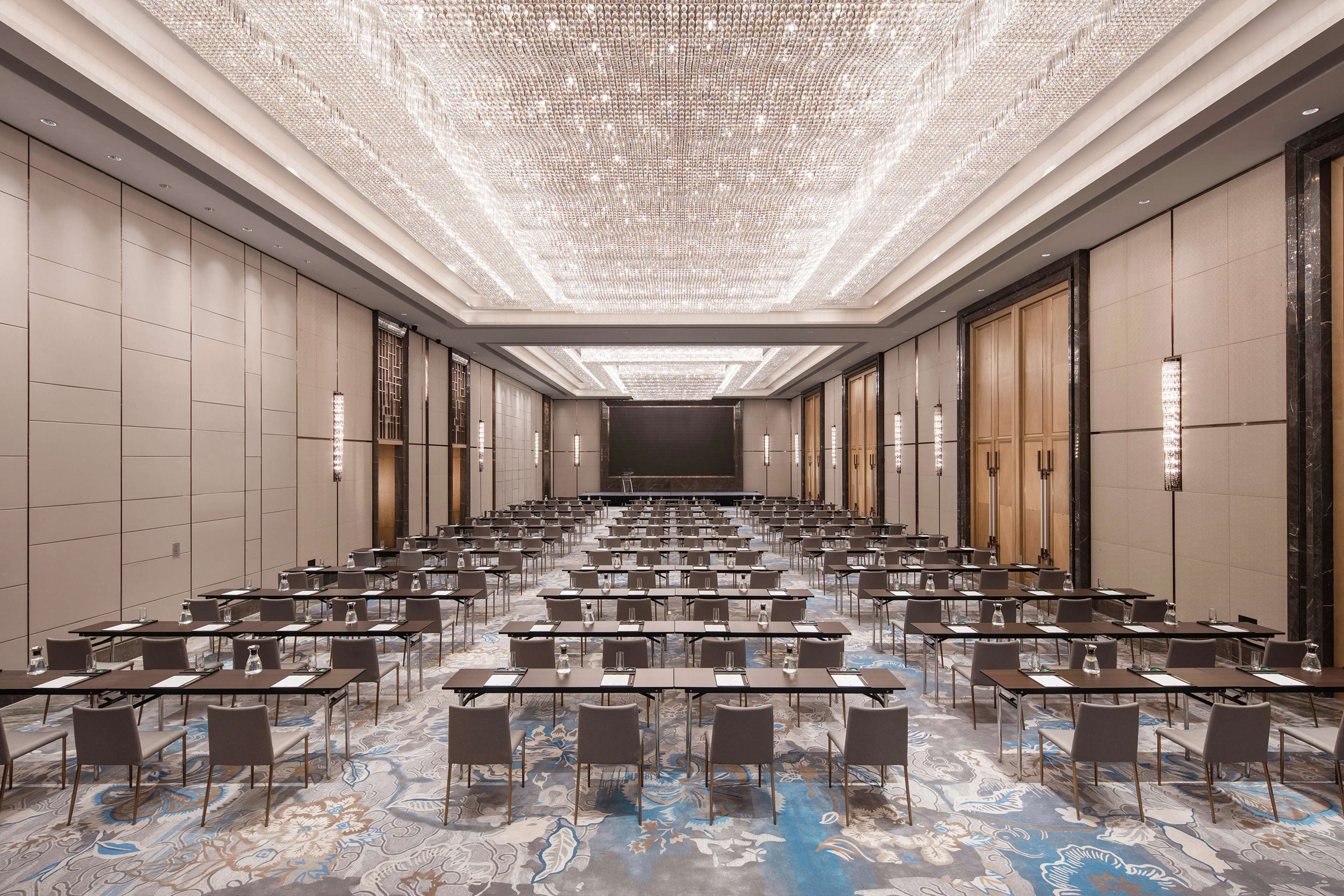 A conference room with rows of tables and chairs, a patterned carpet, and a decorative ceiling.