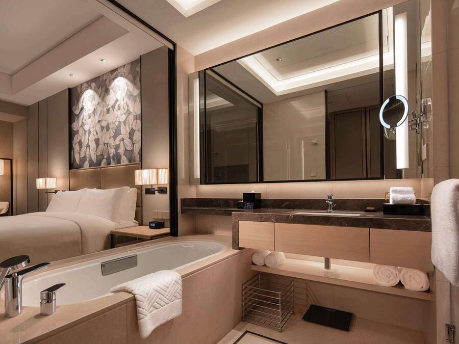 Un baño de hotel moderno con una bañera grande, un tocador con espejo y un espejo grande sobre el lavabo.